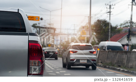 Close up rear side of pickup car silver color. Car is driving in the left lane. And on the right lane there is another car driving with its brake lights on. Road barriers made of large cement. 132641659