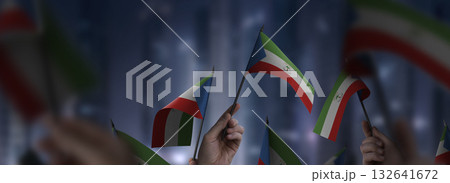 Equatorial Guinea flags in their hands on a blurred urban background Equatorial Guinea flags in their hands on a blurred urban background 132641672