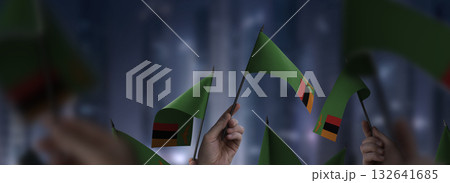 Zambia flags in their hands on a blurred urban background 132641685