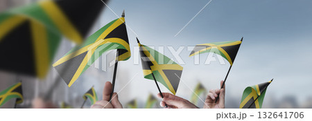 Jamaica flags in their hands on a blurred urban background Jamaica flags in their hands on a blurred urban background 132641706