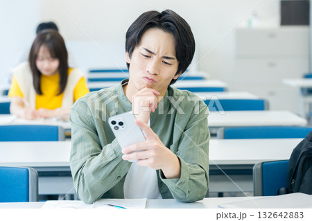 スマホを見ながら悩む大学生 132642883