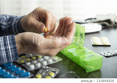 Middle aged caucasian man counts out pills for distributing scheduled dose of medication into pillbox Middle aged caucasian man counts out pills for distributing scheduled dose of medication into pillbox 132643028