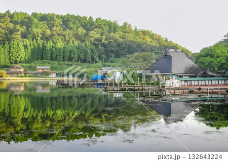 福井県・水月湖の湖畔風景、鏡のような水面に映り込む新緑の山々と伝統的な建物 132643224