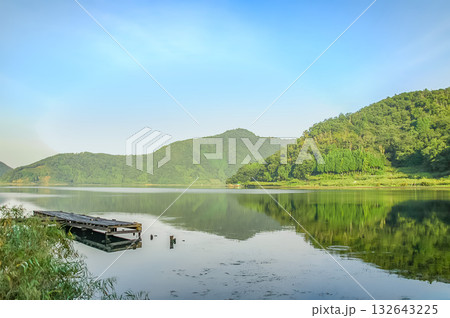 福井県・水月湖の朝、静かな湖面に映り込む新緑の山々と古い桟橋の風景 132643225