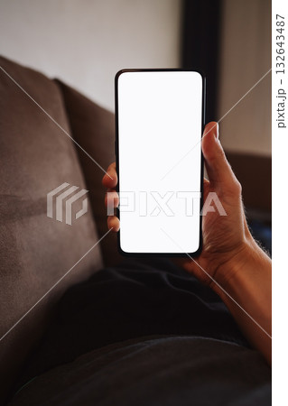 Man hold smartphone with white screen in his hand lying on a couch in home environment 132643487