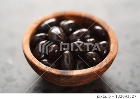 Dark chocolate dragee in olive wood bowl on concrete background 132643527