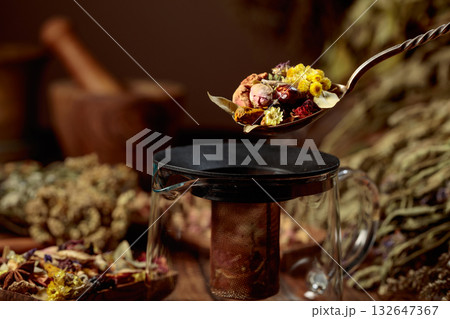 Various dried herbs and spices is poured into a glass teapot. Various dried herbs and spices is poured into a glass teapot. 132647367