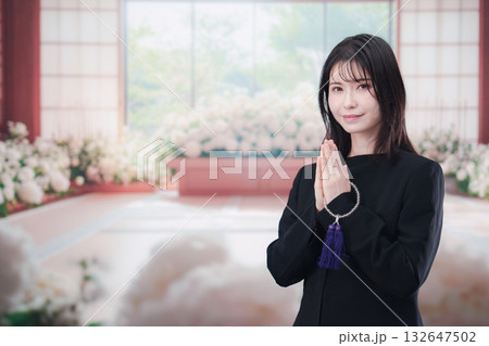 お葬式で合掌をする喪服を着た若い女性 132647502