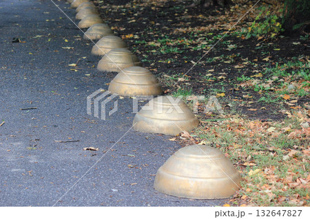 Row of golden dome-shaped bollards on an asphalt path in a park, used for safety and access control Row of golden dome-shaped bollards on an asphalt path in a park, used for safety and access control 132647827