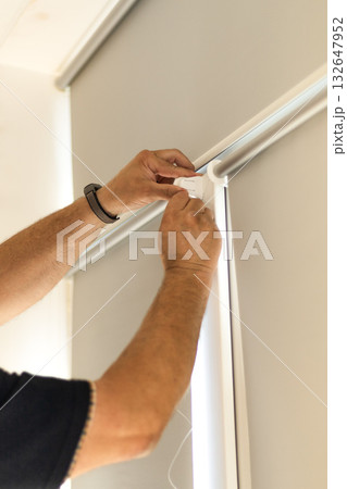 Installation of light gray roller blinds with reflective foil coating on windows. 132647952