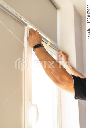 Worker installing roller blinds with reflective coating on windows for sunlight protection. 132647990