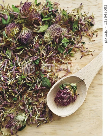 Loose dried red clover flowers and leaves on wooden board with wooden spoon, rustic texture and natural herbal tea mood 132648003