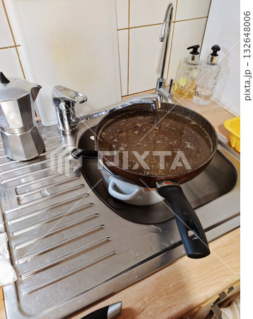 Greasy frying pan soaking in stainless kitchen sink, dish soap and sponge nearby, moka pot and dispenser on counter, everyday cleanup scene 132648006
