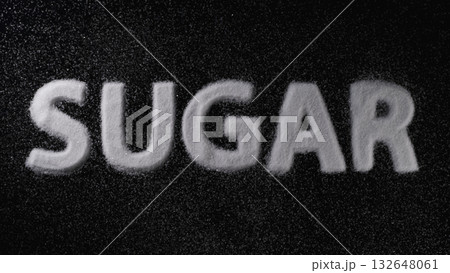 Sugar spelled out with white granules on a dark surface showcasing the texture and contrast of the material Sugar spelled out with white granules on a dark surface showcasing the texture and contrast of the material 132648061