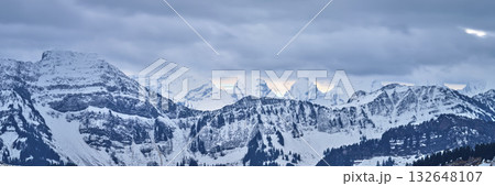 Snow-covered mountain range under a cloudy sky during the late afternoon Snow-covered mountain range under a cloudy sky during the late afternoon 132648107