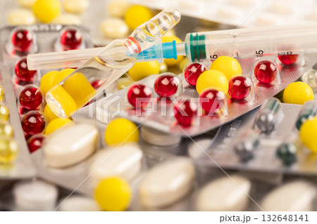 Multicolored tablets and capsules on the table. Ampoule and syringe for injections. Multicolored tablets and capsules on the table. Ampoule and syringe for injections. 132648141
