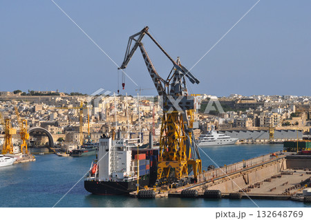 Valletta, Malta : Cargo cranes and large ship docked near sandstone fortifications and boats in the harbor. Valletta, Malta : Cargo cranes and large ship docked near sandstone fortifications and boats in the harbor. 132648769