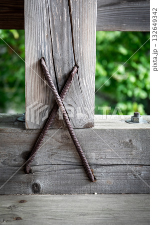 Detailed view of weathered wooden beam reinforced with crossed rusty steel rods Detailed view of weathered wooden beam reinforced with crossed rusty steel rods 132649342