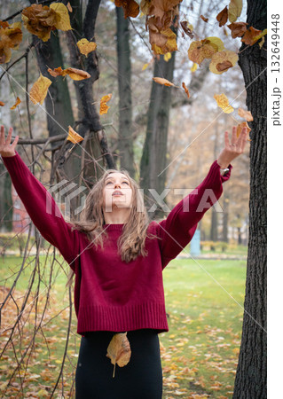 Teenage girl in a red sweater throws autumn leaves into the air in a park, enjoying the moment of freedom and playfulness Teenage girl in a red sweater throws autumn leaves into the air in a park, enjoying the moment of freedom and playfulness 132649448