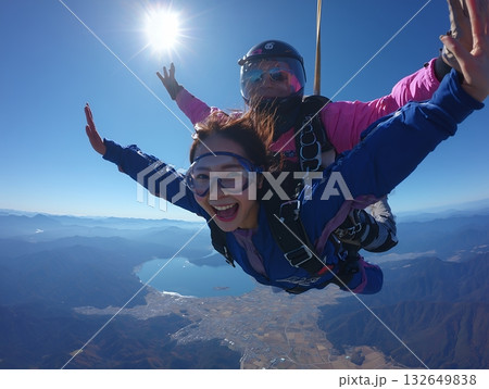 青空と太陽の下で雄大な山と湖を背景にタンデムスカイダイビングを楽しむ笑顔の日本人女性 青空と太陽の下で雄大な山と湖を背景にタンデムスカイダイビングを楽しむ笑顔の日本人女性 132649838