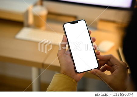 Close up of man hands holding mock up smart phone with modern workspace Close up of man hands holding mock up smart phone with modern workspace 132650374