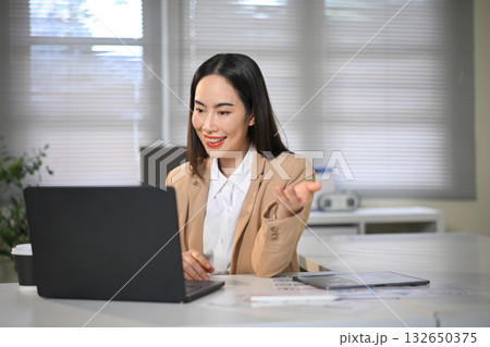 Middle aged businesswoman using laptop in modern office, focusing on work and analysis with confidence and professionalism. 132650375