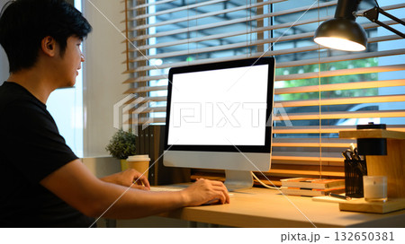 Man working on desktop computer in home office with coffee cup and warm light Man working on desktop computer in home office with coffee cup and warm light 132650381