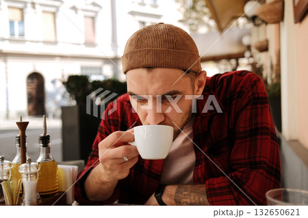 Focused young man sipping hot cappuccino at an outdoor cafe on a sunny day Focused young man sipping hot cappuccino at an outdoor cafe on a sunny day 132650621