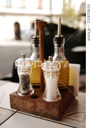 Elegant condiments set with olive oil, salt, and pepper in glass bottles on bright restaurant table Elegant condiments set with olive oil, salt, and pepper in glass bottles on bright restaurant table 132650626