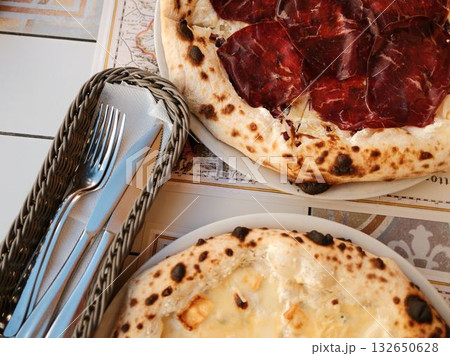 Freshly baked two pizza with golden cheese next to basket of cutlery, ready for perfect dining experience. Italian outdoor cafe, close view Freshly baked two pizza with golden cheese next to basket of cutlery, ready for perfect dining experience. Italian outdoor cafe, close view 132650628