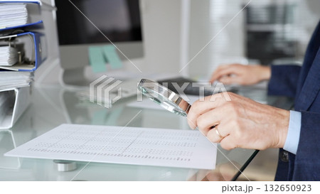 Hand holding magnifying glass, inspecting financial document, performing audit and business analysis. Audit and taxes in business Hand holding magnifying glass, inspecting financial document, performing audit and business analysis. Audit and taxes in business 132650923