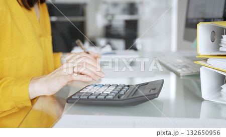 Woman in yellow blouse calculating finances, managing budget, doing taxes, working on accounting documents in office workspace. Audit and taxes in business Woman in yellow blouse calculating finances, managing budget, doing taxes, working on accounting documents in office workspace. Audit and taxes in business 132650956