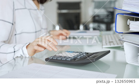Professional woman calculating financial data using black calculator on office desk, managing expenses and budget. Audit and taxes in business 132650965