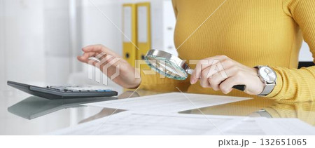 Woman auditing financial documents using magnifying glass and calculator, checking details, managing finance in office. Audit and taxes in business Woman auditing financial documents using magnifying glass and calculator, checking details, managing finance in office. Audit and taxes in business 132651065