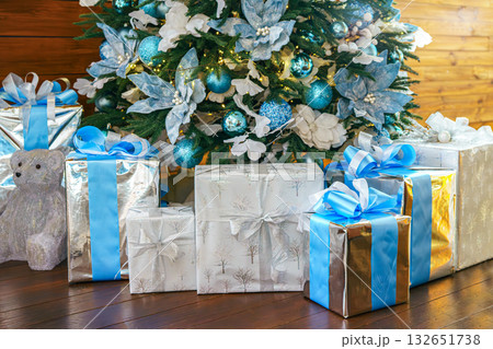 Beautifully wrapped gifts under a festive Christmas tree with blue accents ornaments Beautifully wrapped gifts under a festive Christmas tree with blue accents ornaments 132651738