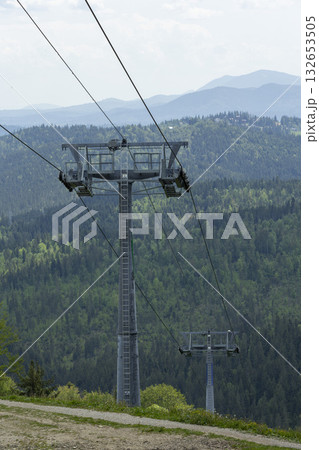 Cable car supports, chairlift hangs over a green mountain valley 132653505