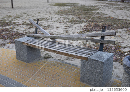 A broken wooden bench stands on a brick path A broken wooden bench stands on a brick path 132653600