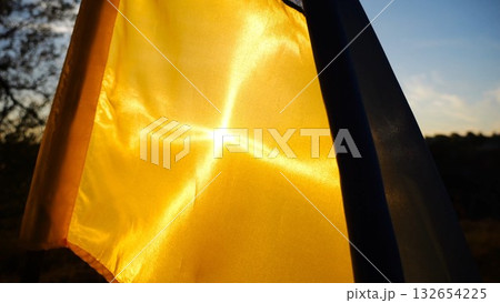 Blue-yellow symbol of Ukraine waving at wind against the background of sunlight. Ukrainian flag illuminated by sun fluttering at countryside. Concept of peace and support against russian aggression Blue-yellow symbol of Ukraine waving at wind against the background of sunlight. Ukrainian flag illuminated by sun fluttering at countryside. Concept of peace and support against russian aggression 132654225