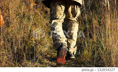 Low view to male feet of ukrainian soldiers going along trail at countryside. Legs of young army man walking through dry grass at sunny day. War in Ukraine. Slow motion 132654227