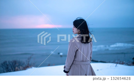 ロングコートの若い日本人女性 雪の降る海辺で海を見つめる冬の夜 132654628