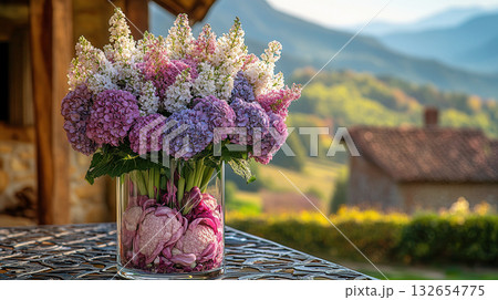 Glass vase with vibrant arrangement of pink and white hydrangea flowers, filled with purple cabbage leaves at bottom, placed outdoors with golden hour light in background. 132654775