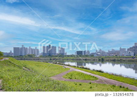 青空と白い雲、緑豊かな河川敷から望む都市景観 青空と白い雲、緑豊かな河川敷から望む都市景観 132654878