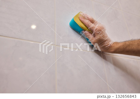 A Man Diligently Cleaning a Tiled Bathroom Wall with His Gloves and a Scrubber Tool A Man Diligently Cleaning a Tiled Bathroom Wall with His Gloves and a Scrubber Tool 132656843