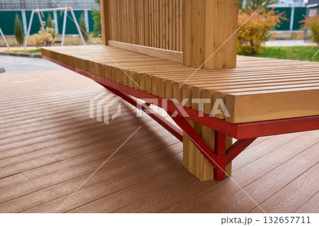 Wooden bench outdoors, Outdoor wooden bench with metal accents, Comfortable timber seating on urban plaza, Charming outdoor bench featuring red supports and warm wooden 132657711