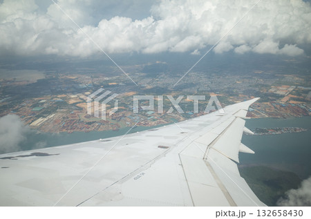 下降中の旅客機の窓際席から翼越しに望む雲と下界の街並み 132658430