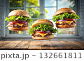 Three appetizing cheeseburgers floating midair above a wooden surface 132661811