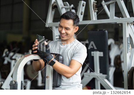 Joyful Workout. Man smiling at smartphone while resting at gym. 132662654