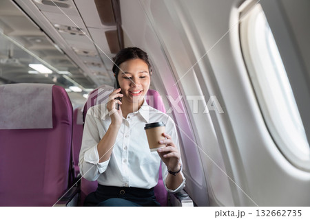 Business travel: Smiling woman on the phone with coffee in airplane 132662735