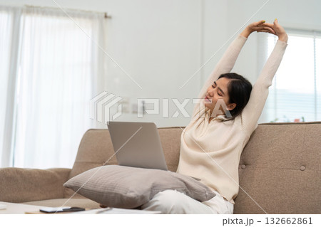 Remote Work and Relaxation. A woman stretching at home while working on her laptop, balancing productivity and comfort. 132662861