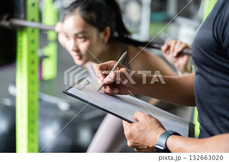 Fitness Assessment. Trainer recording performance of young woman during squat exercise. Fitness Assessment. Trainer recording performance of young woman during squat exercise. 132663020